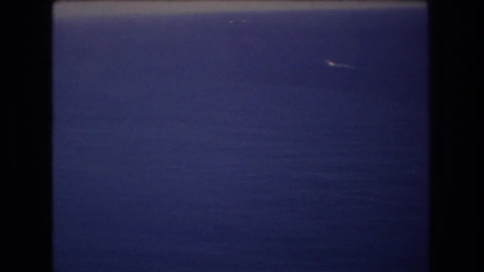 1977 8mm frame from near Honolulu showing deep blue ocean, a pale horizon band, and a small white distant object or wake against the water.