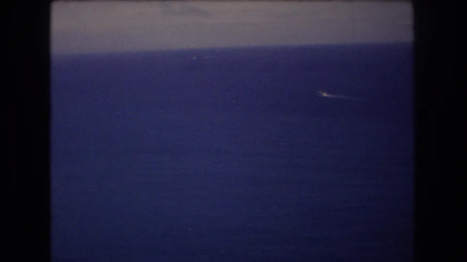 1977 8mm frame near Honolulu with open ocean filling the view and a small white speck or wake near the distant horizon.