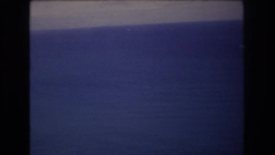 1977 8mm frame near Honolulu showing mostly uninterrupted blue ocean, a pale horizon or cloud band, and dark film gate borders.