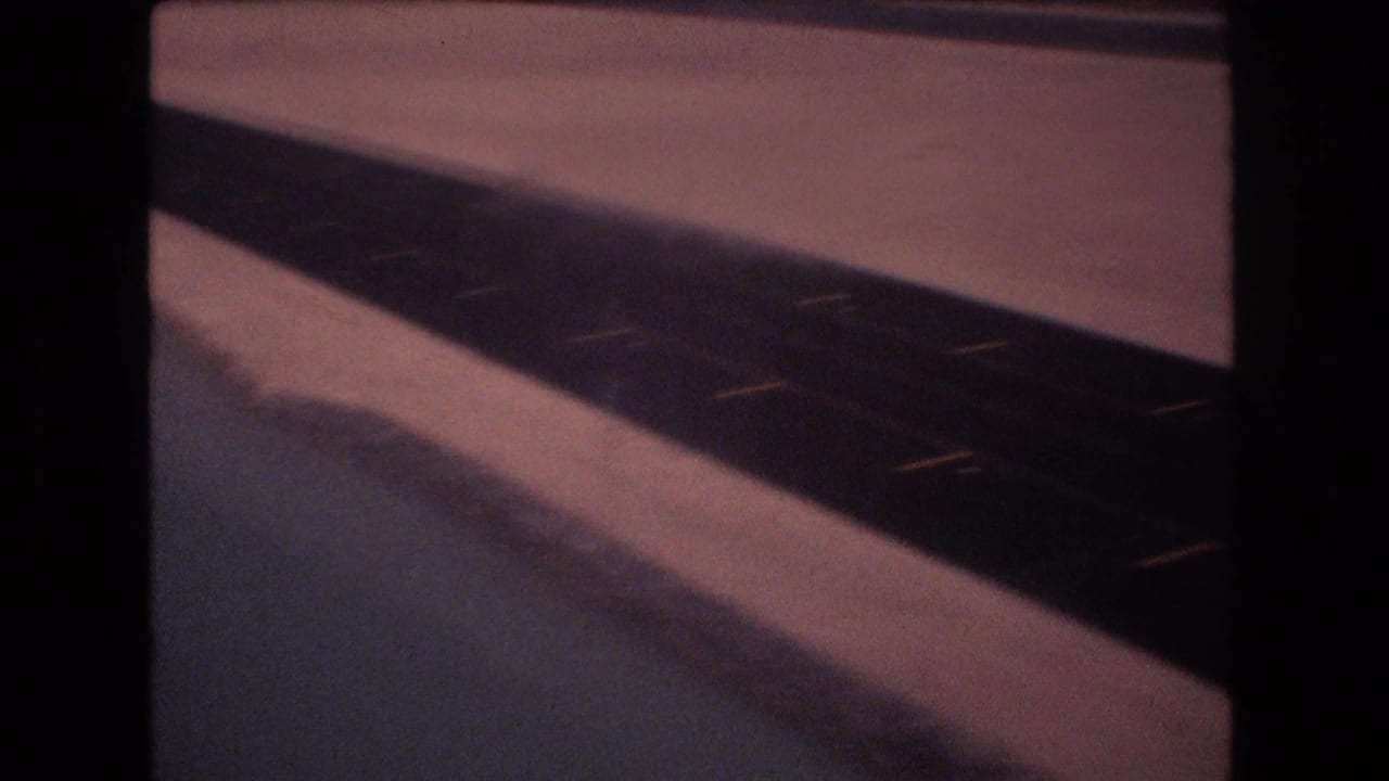 1977 8mm home-movie frame from the Honolulu Hawaii reel showing a low, bumpy view past a dark road or track edge and pale arid ground.