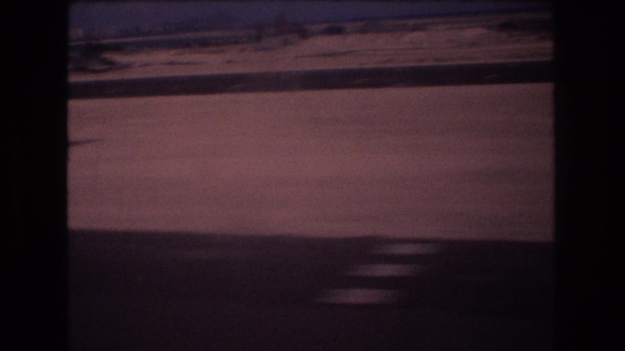 Blurred moving-vehicle view of pavement or shoulder with a low horizon and dark foreground frame.