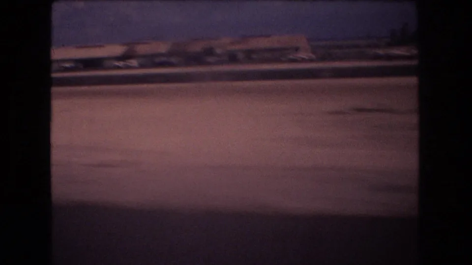 A final 8mm frame shows the moving vehicle passing a flat roadside landscape with low distant structures, a few trees, and strong magenta color shift.