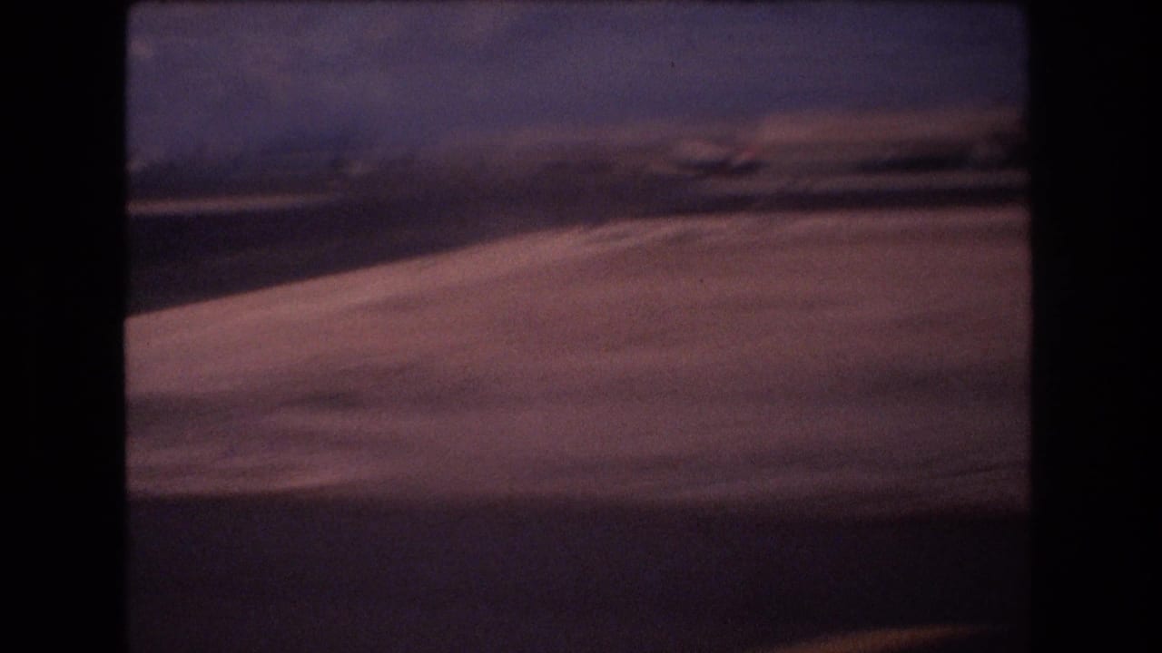 Low view along a runway or taxiway with a blurred wing edge and distant aircraft shape.