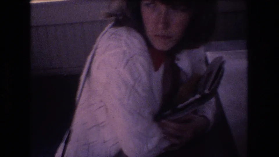 At the end of the Honolulu home-movie clip, the woman faces toward the camera from an indoor seat while still holding a book or magazine against her cardigan.