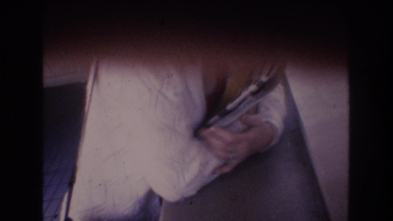 Soft 8mm frame from the Honolulu 1977 home movie showing a close view of hands with papers before the outdoor lei greeting sequence.
