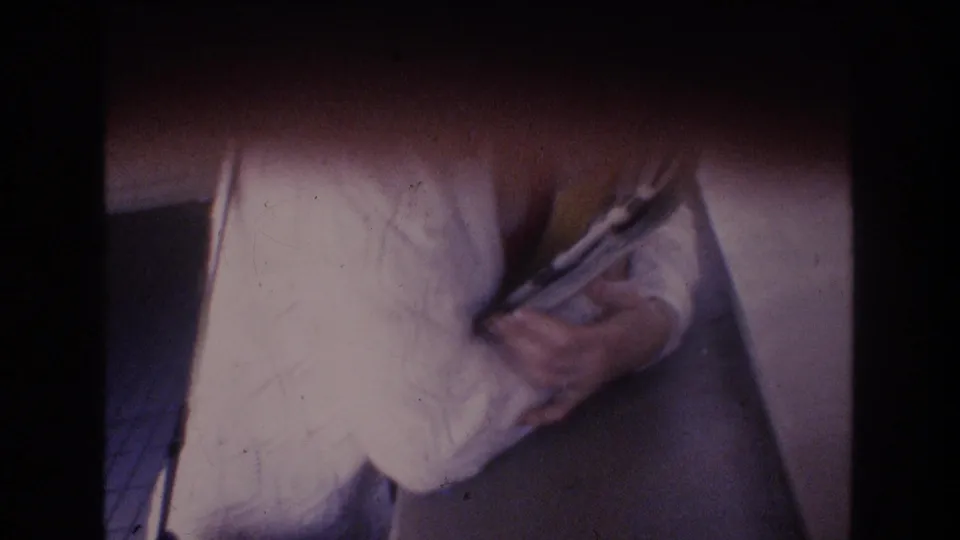 Soft 8mm frame from the Honolulu 1977 home movie showing a close view of hands with papers before the outdoor lei greeting sequence.