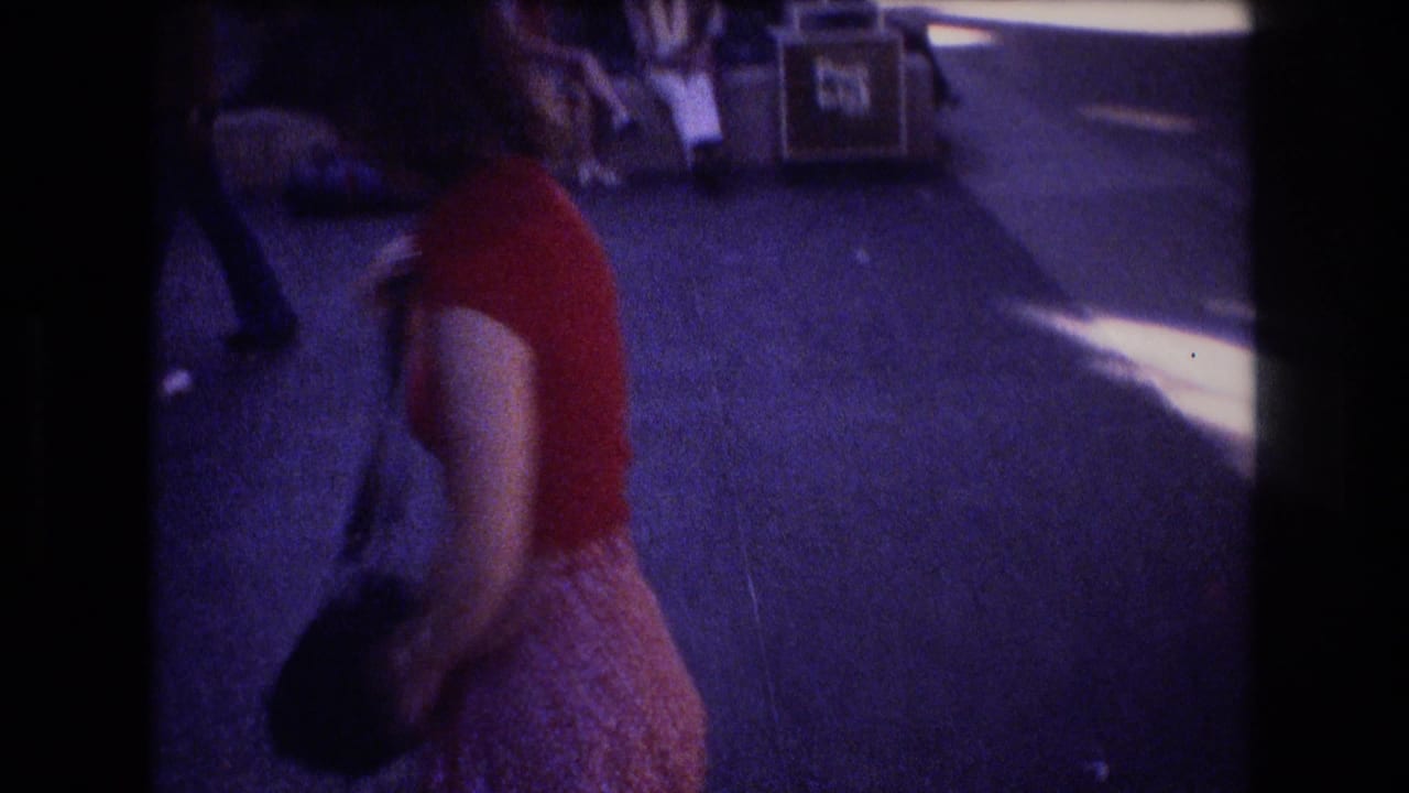 Woman in a red top walking outdoors with a black shoulder bag.