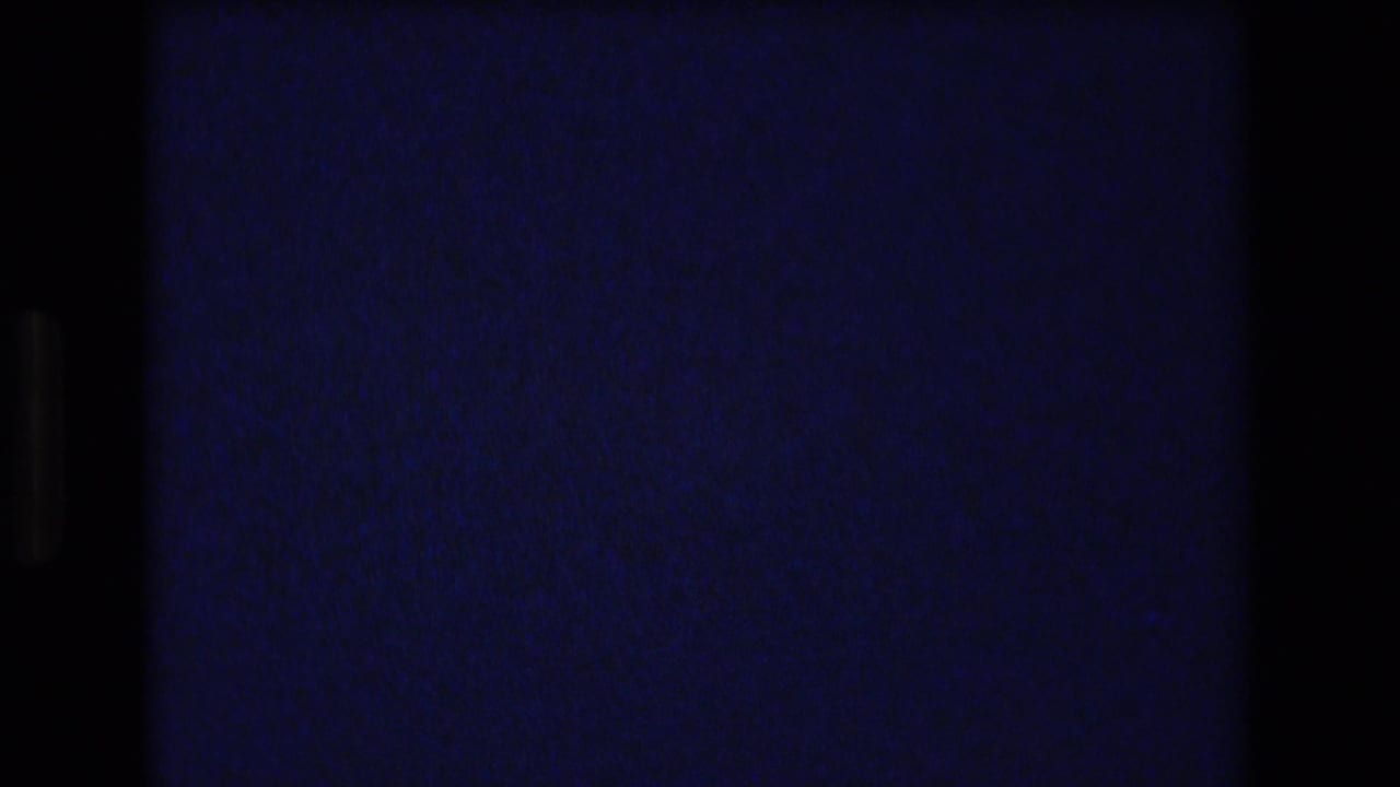 Underexposed opening frame from 1977 8mm Honolulu footage, mostly dark with blue-purple film cast and visible scan borders.