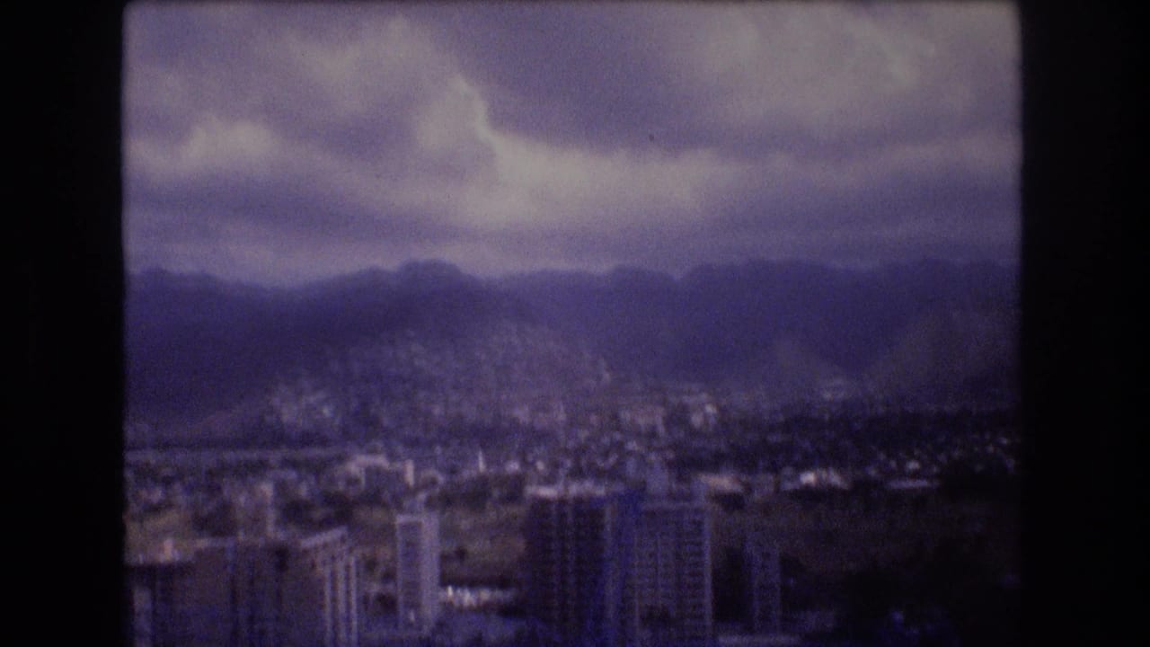 City buildings below dark mountain ridges under heavy clouds.