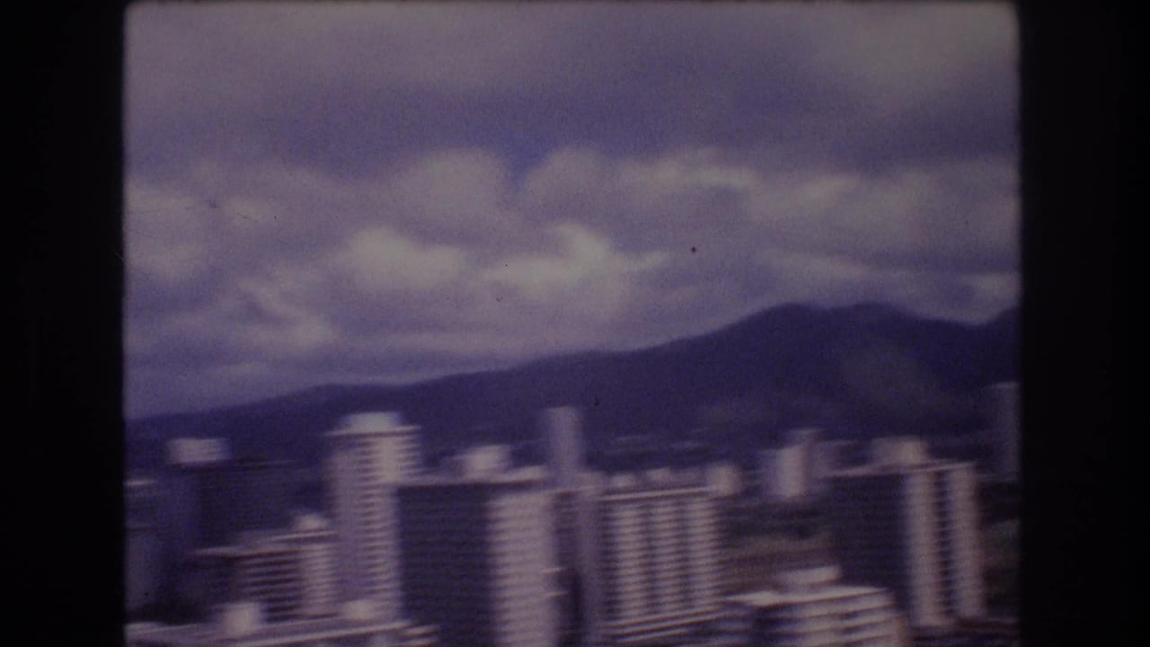 Tall downtown buildings in front of hills beneath a cloudy sky.