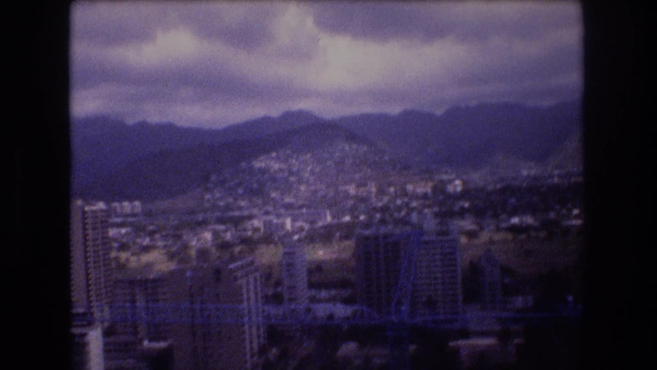 City neighborhoods and high-rises spread across hills below a cloudy mountain backdrop.