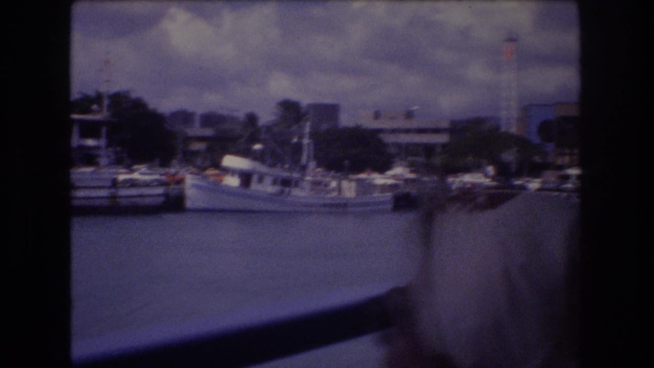 Boat-tour view across harbor water with docked vessels, buildings, rail, and a passenger edge in frame.