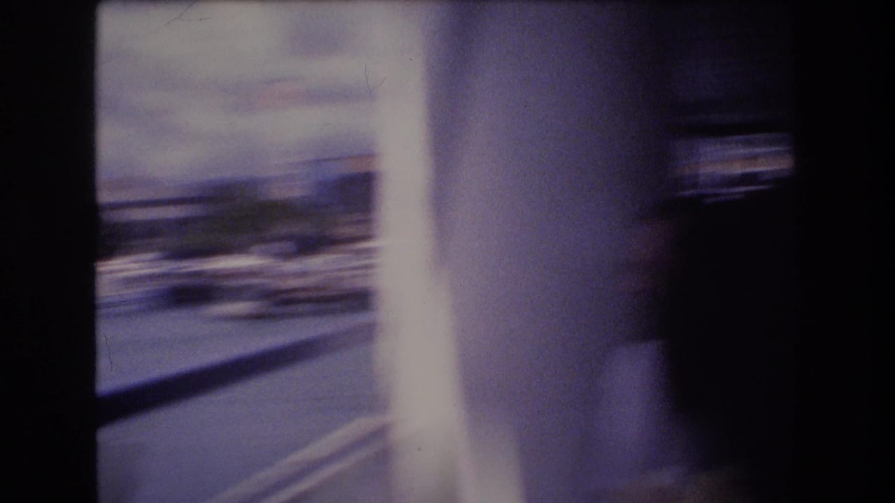 Blurred 8mm frame from the start of the Honolulu harbor clip, showing a dark onboard edge, bright vertical light, and indistinct waterfront forms beyond.