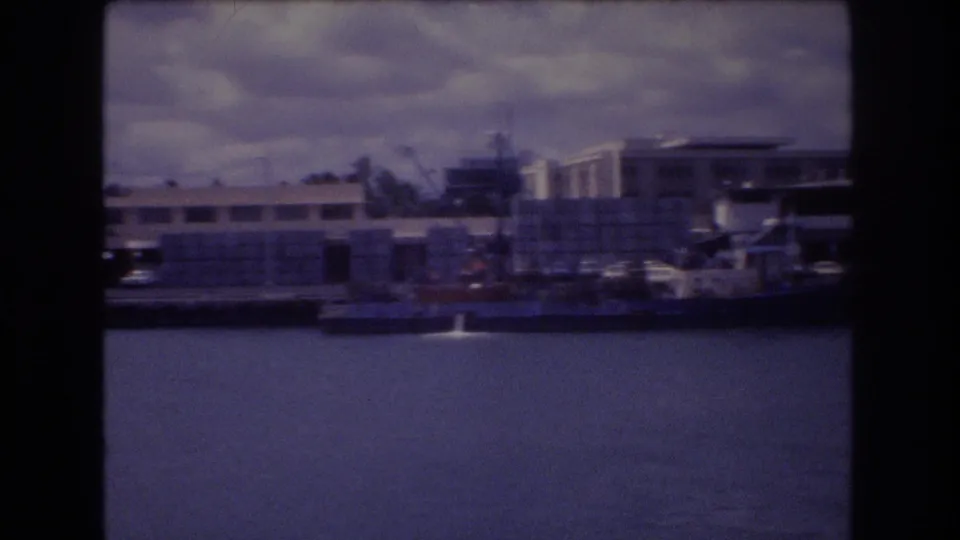 Soft 8mm harbor frame showing calm water, dock structures, small boats, and low waterfront buildings in Honolulu, Hawaii, as described by the clip metadata.