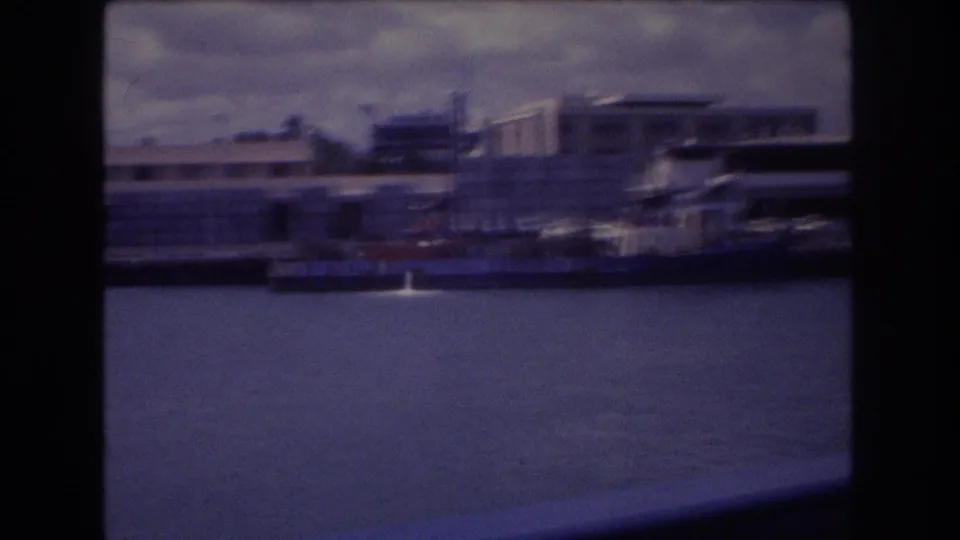 End frame of the 1977 Honolulu home-movie clip, showing a handheld pan across harbor water, docked boats, and waterfront buildings with noticeable motion blur.