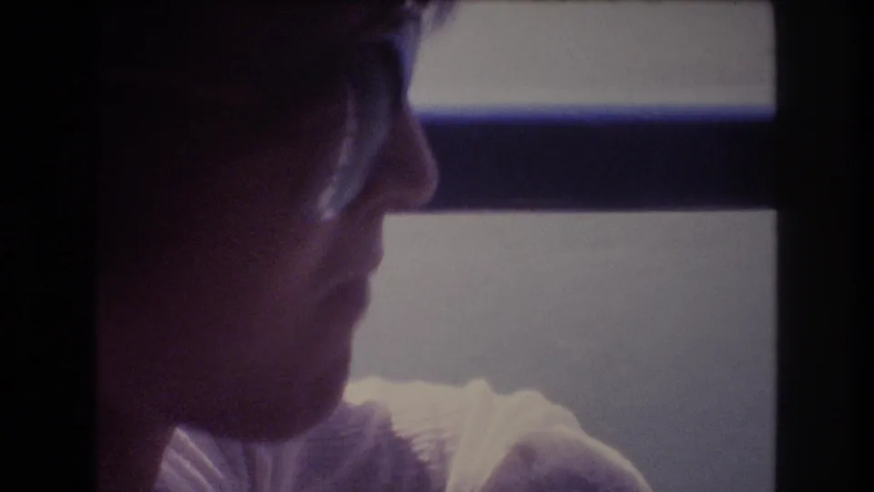 A woman in profile sits or stands near a ship window during a 1977 Honolulu sightseeing moment, with water and dark window framing behind her.