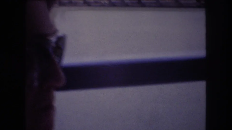 A woman in profile wearing glasses sits beside a dark-framed boat window during a 1977 Honolulu home-movie travel scene.