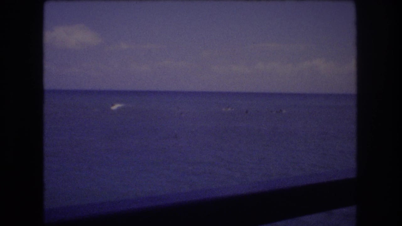 Blue ocean and cloudy sky with a small white wake visible near the distant horizon.