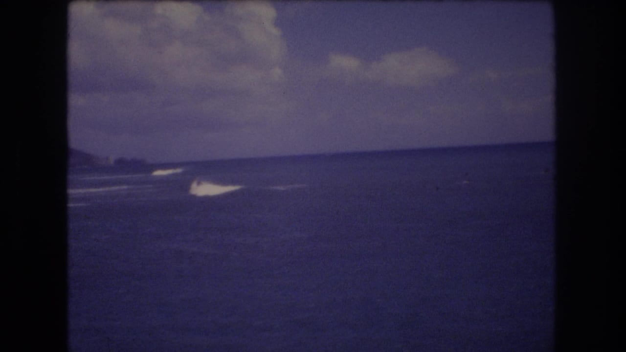 1977 Honolulu home-movie frame showing open ocean, a low horizon, distant surf, and a cloudy sky with soft 8mm color fading.