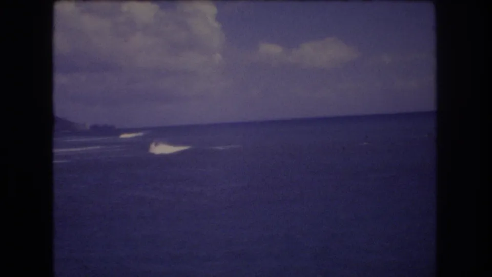 1977 Honolulu home-movie frame showing open ocean, a low horizon, distant surf, and a cloudy sky with soft 8mm color fading.