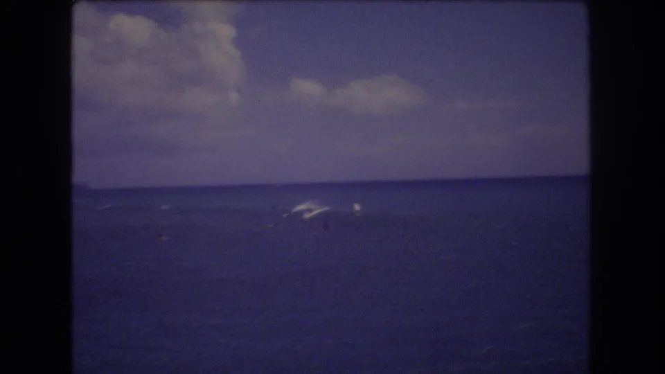1977 Honolulu home-movie frame with small wave breaks in the distance, open Pacific water, a low horizon, and soft cloud forms overhead.