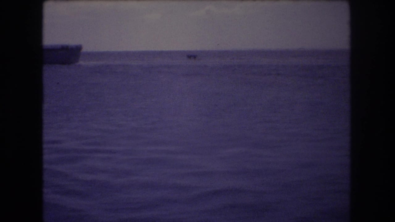 1977 Honolulu 8mm frame showing calm open ocean, a muted sky, a distant boat near the horizon, and a larger vessel partly entering from the left edge.