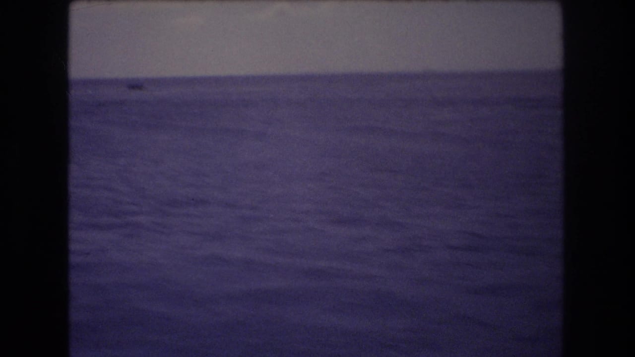 1977 Honolulu home-movie frame showing a broad expanse of ocean water beneath a dim, hazy sky, with dark 8mm frame edges visible.