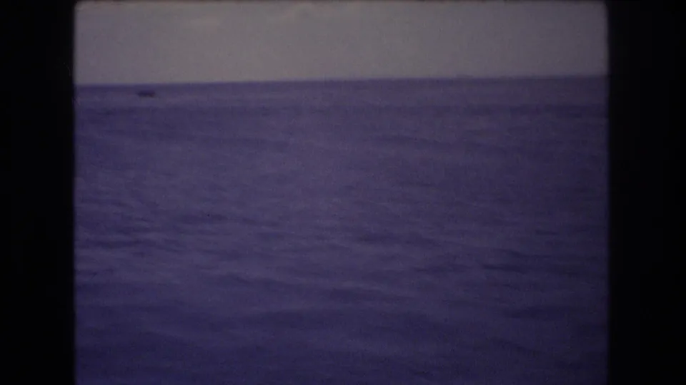 1977 Honolulu home-movie frame showing a broad expanse of ocean water beneath a dim, hazy sky, with dark 8mm frame edges visible.