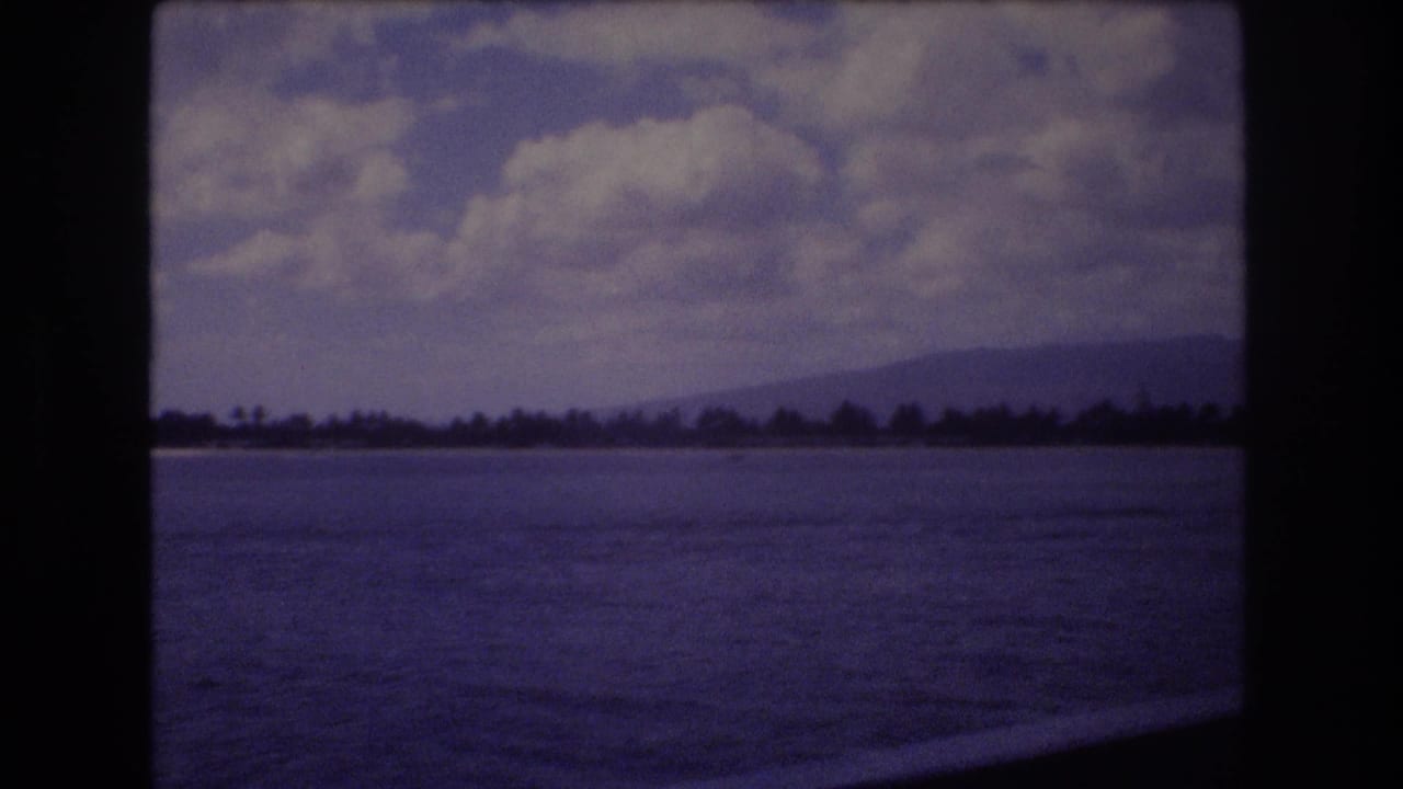 Open water beneath a cloudy sky with shoreline and mountains on the horizon.