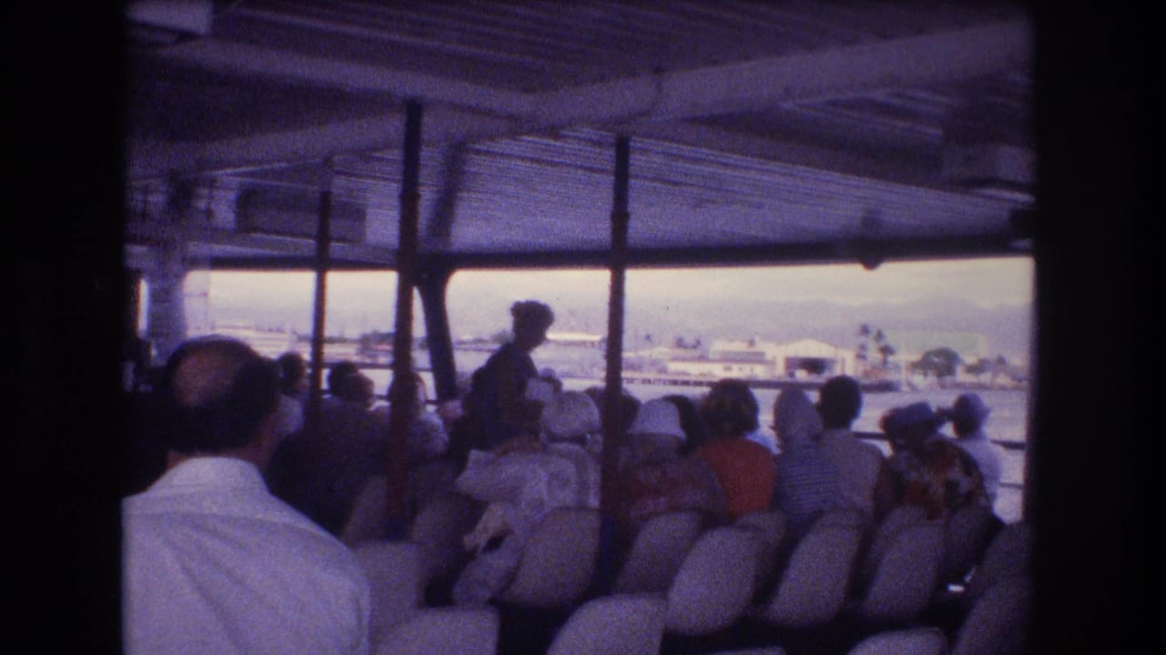 Rows of passengers sit under a covered vessel roof while a standing figure faces the open side.