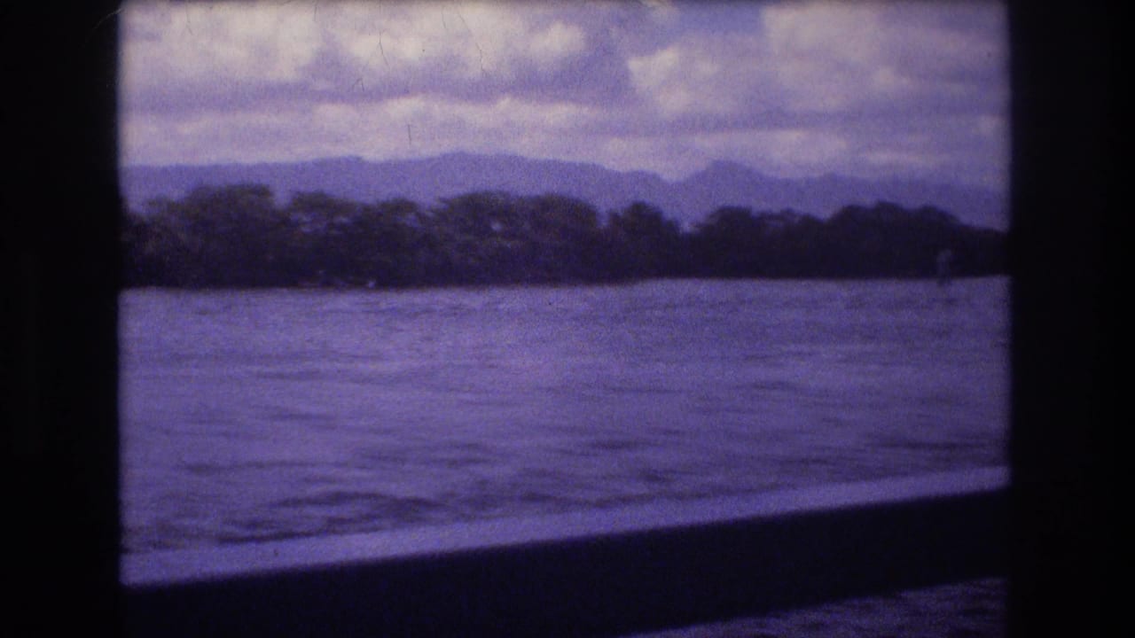 Water and distant wooded shoreline seen through a dark window frame under layered clouds.