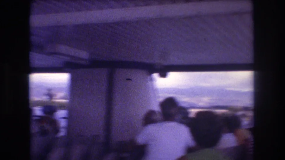 Interior ferry view in Honolulu with passengers facing outward, including a man in a white shirt, beneath an overhead panel with water and sky visible beyond.