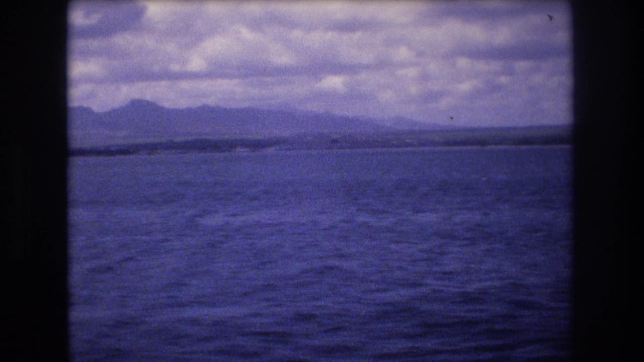 Blue ocean and distant hilly shoreline beneath a cloudy sky.