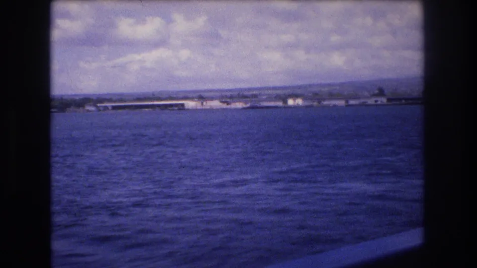 A panning 8mm frame shows a broad expanse of water with low buildings or shoreline structures across the horizon in Honolulu, Hawaii, according to the clip metadata.
