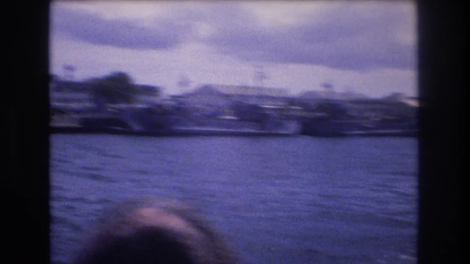 1977 Honolulu 8mm frame showing water and a distant shoreline from a moving boat, with a partial passenger head entering the lower edge.
