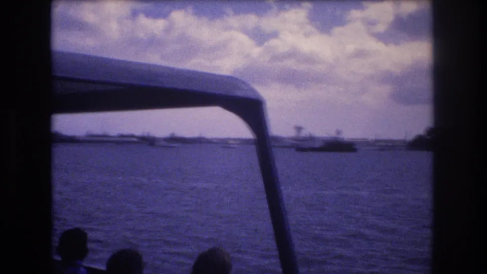 Honolulu 8mm travel footage widens to open water, with the boat canopy in the foreground, distant vessels and shoreline, and partial passenger silhouettes at the bottom edge.