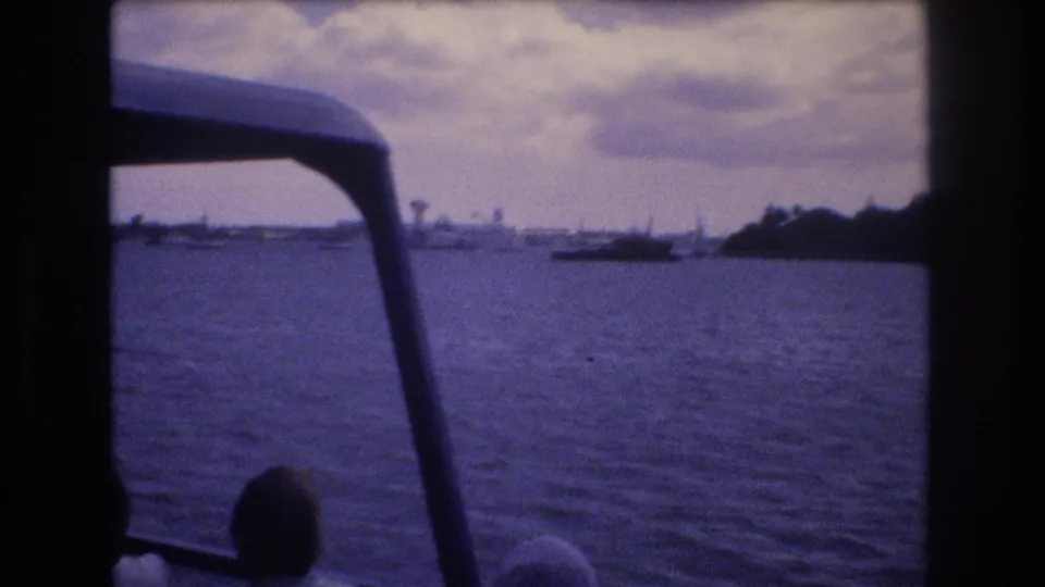1977 Honolulu boat-tour footage showing water, horizon structures, small boats, and silhouetted passengers beneath the dark edge of the vessel canopy.