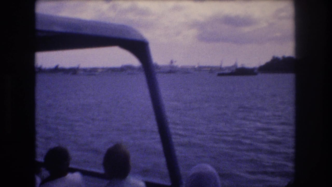 Boat-window view of open water, shoreline, and seated passenger silhouettes.