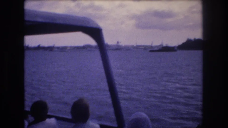 1977 Honolulu boat-ride frame showing open water and distant coast through the vessel structure, with passenger silhouettes at the lower edge.