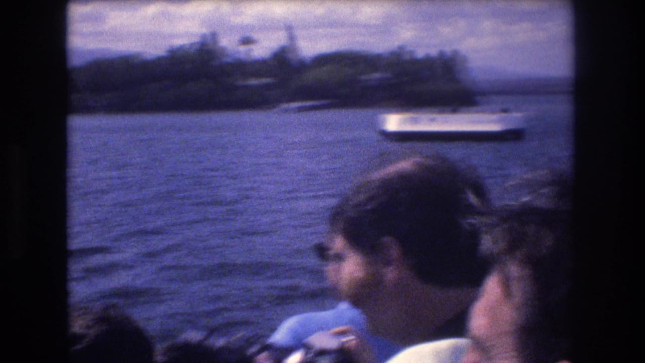 Passengers sit by a boat window with harbor water and a white boat beyond them.