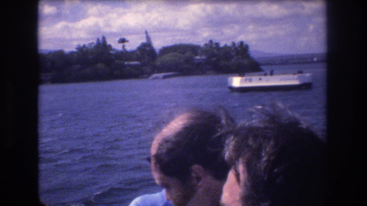 In 1977 Honolulu home-movie footage, passengers on a boat look toward blue water, a tree-lined shoreline, and a small white vessel passing in the distance.