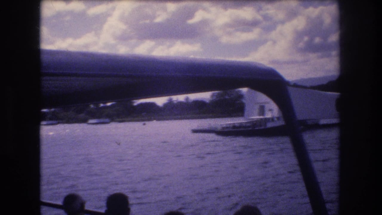 Boat canopy and rail frame the memorial and harbor water with several distant silhouettes at the bottom edge.
