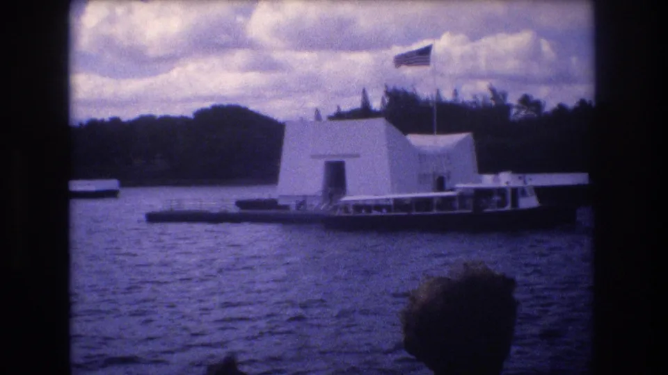 A tour boat passes near the USS Arizona Memorial in Honolulu while a foreground passenger head enters the lower frame, emphasizing the visitor-shot boat perspective.