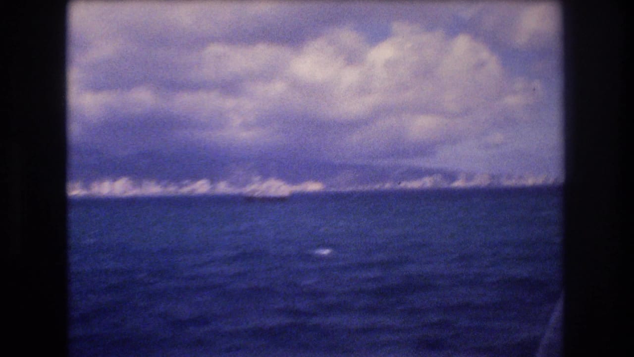 Open ocean with a distant bright shoreline and cloud-filled sky.