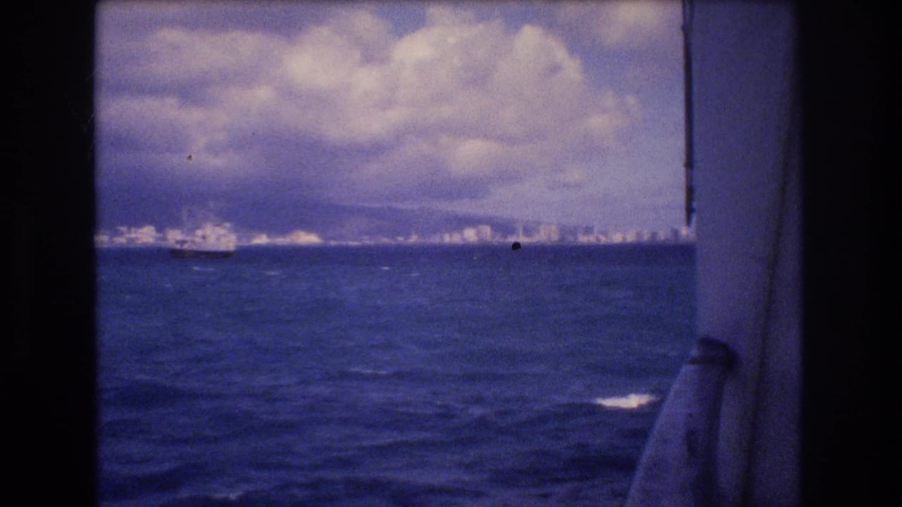 Distant city and mountains across the ocean seen through dark ship framing.