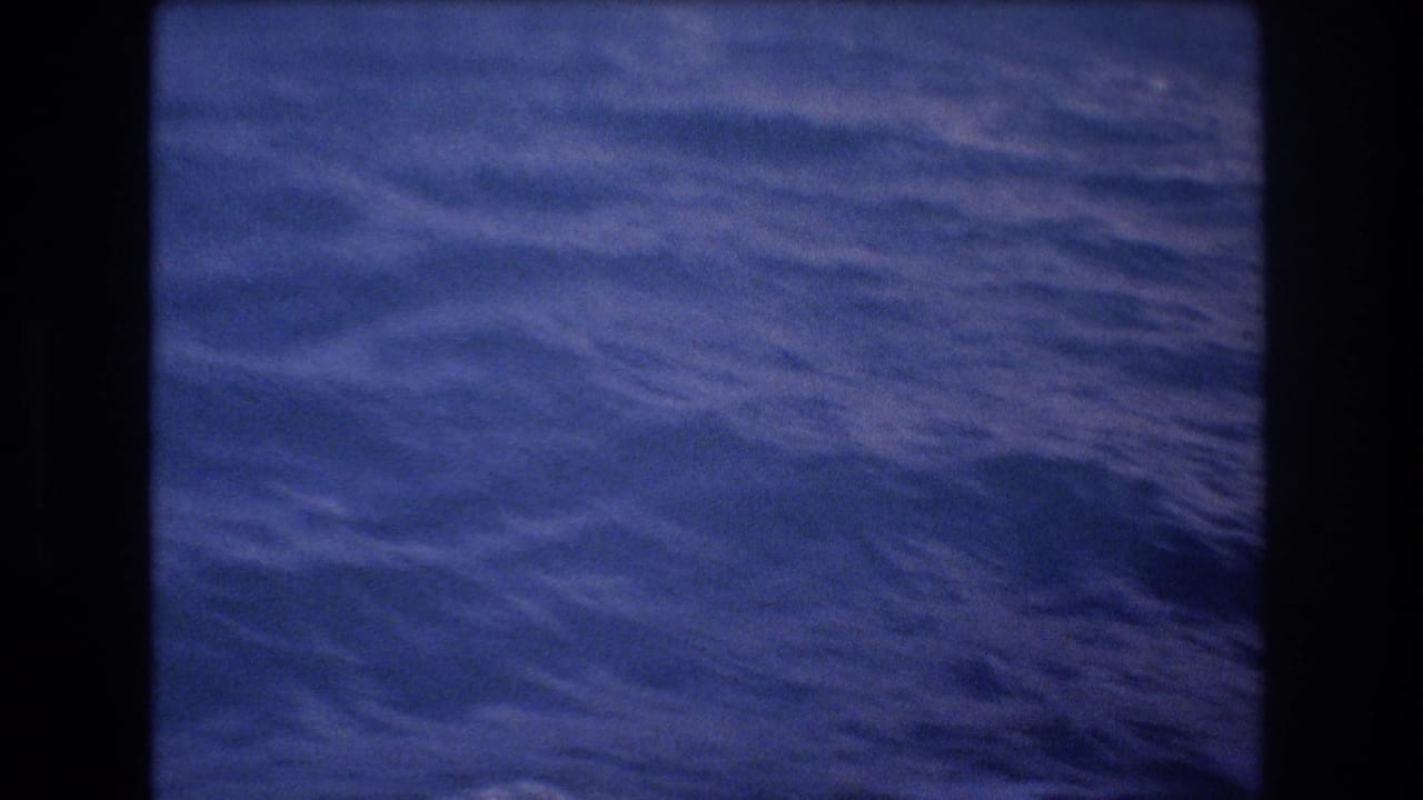 1977 8mm Honolulu-area home-movie frame showing rippled blue ocean water from a moving boat, with soft focus and dark gate edges.