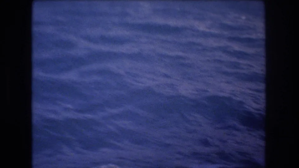 1977 8mm Honolulu-area home-movie frame showing rippled blue ocean water from a moving boat, with soft focus and dark gate edges.