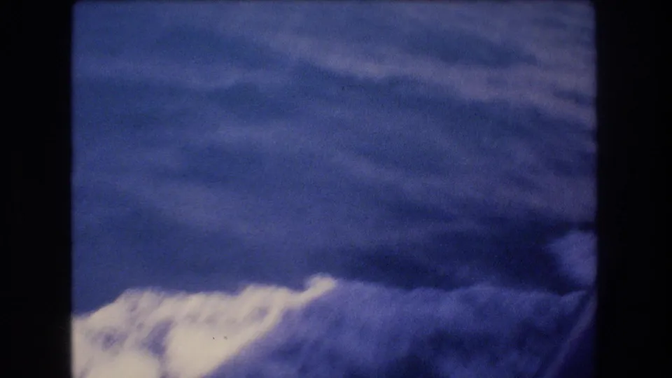 Home-movie view of bright boat wake or wave foam under a cloudy sky, consistent with a short 1977 Honolulu boat sequence.