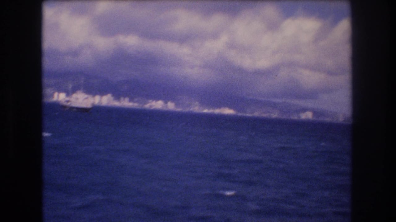 Distant coastline across blue ocean under a cloudy sky with dark frame borders.