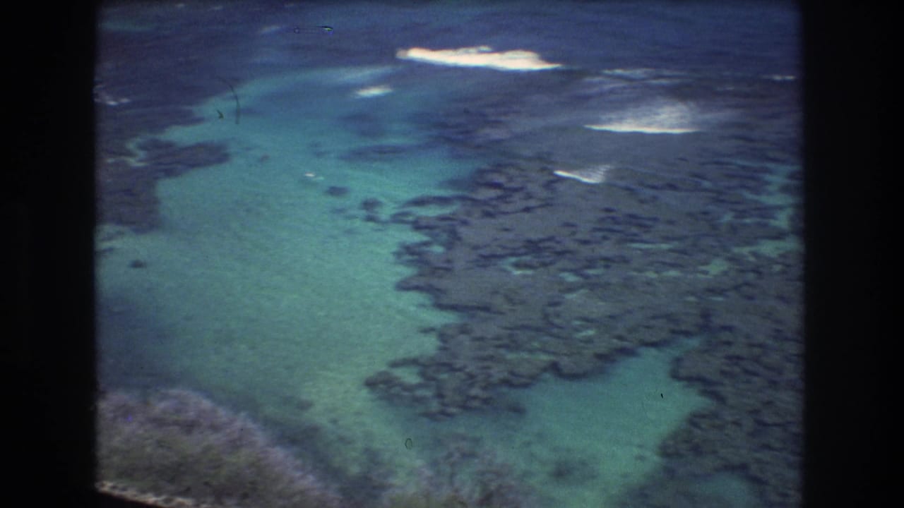 Shallow turquoise sea with dark rock formations and white surf patches.